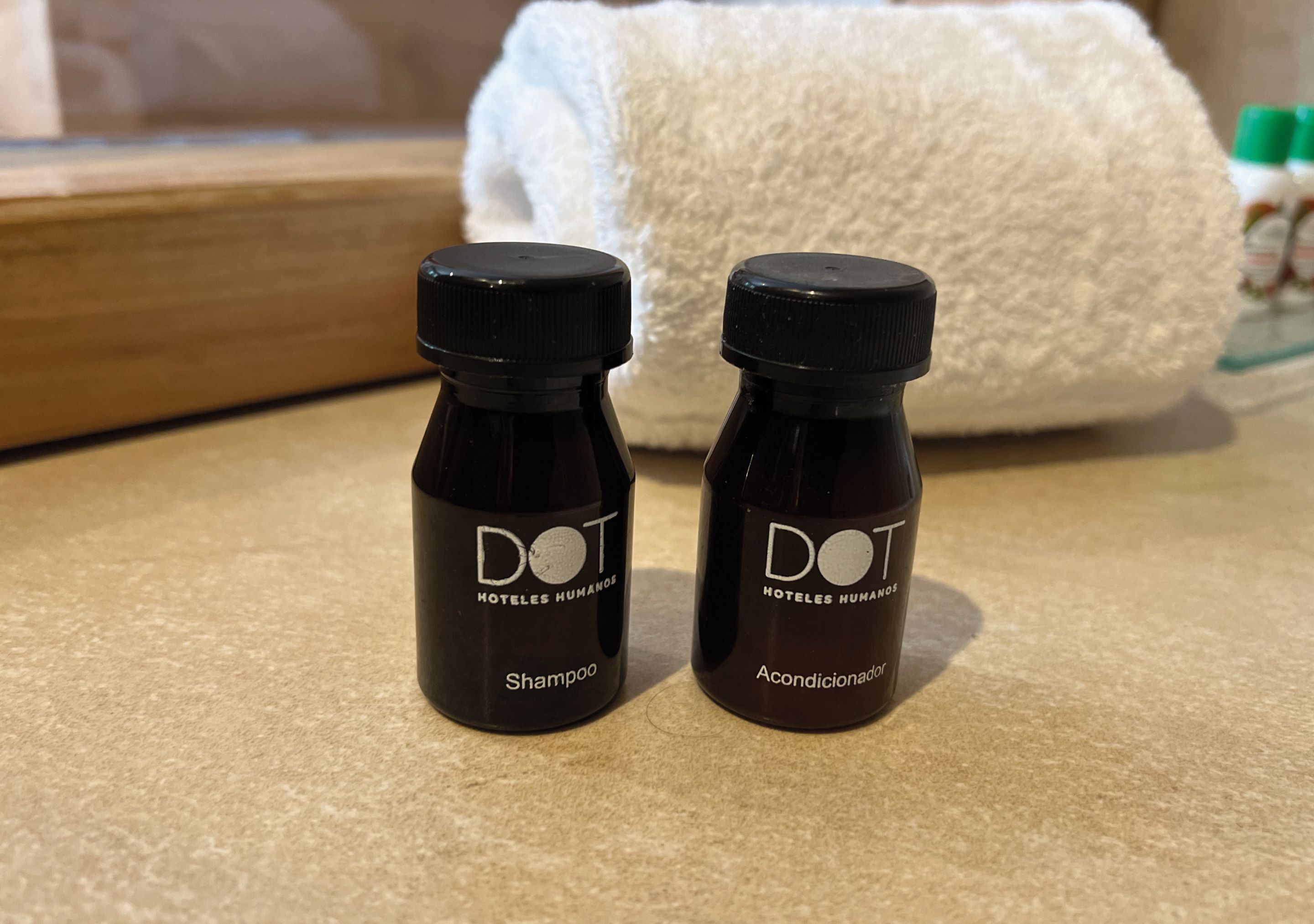 Two small bottles labeled 'DOT' on a countertop, with a white towel and a wooden tray in the background.