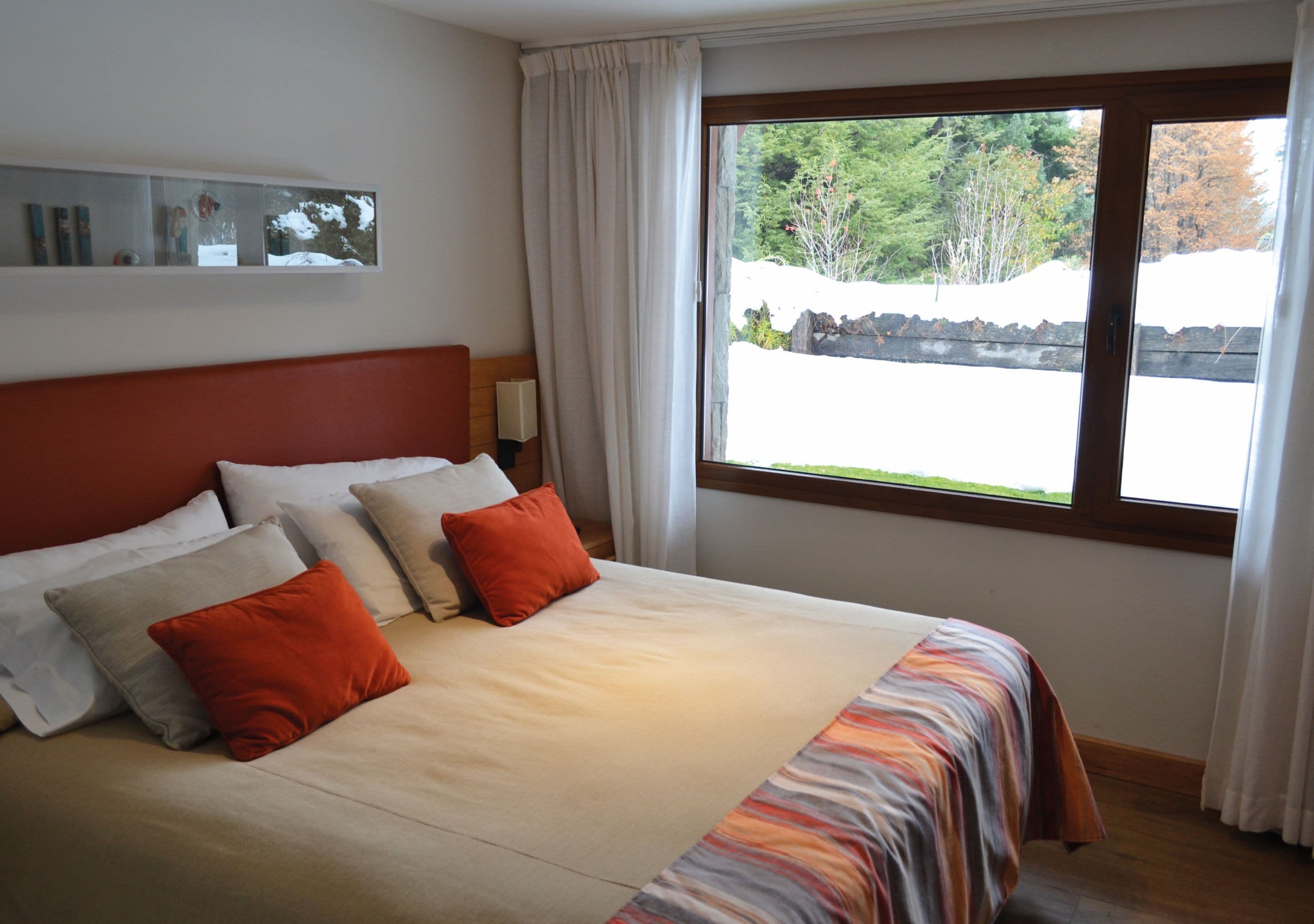 Un dormitorio con una cama grande, cabecera, ventana con cortinas y un espejo en la pared.