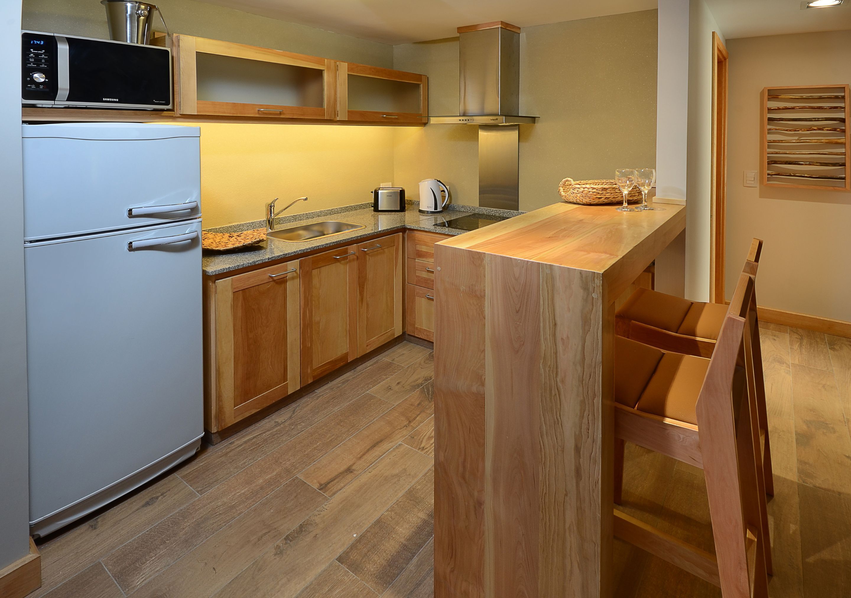 A kitchen with wooden cabinets, a white refrigerator, a microwave, a toaster, and a wooden island with a sink.