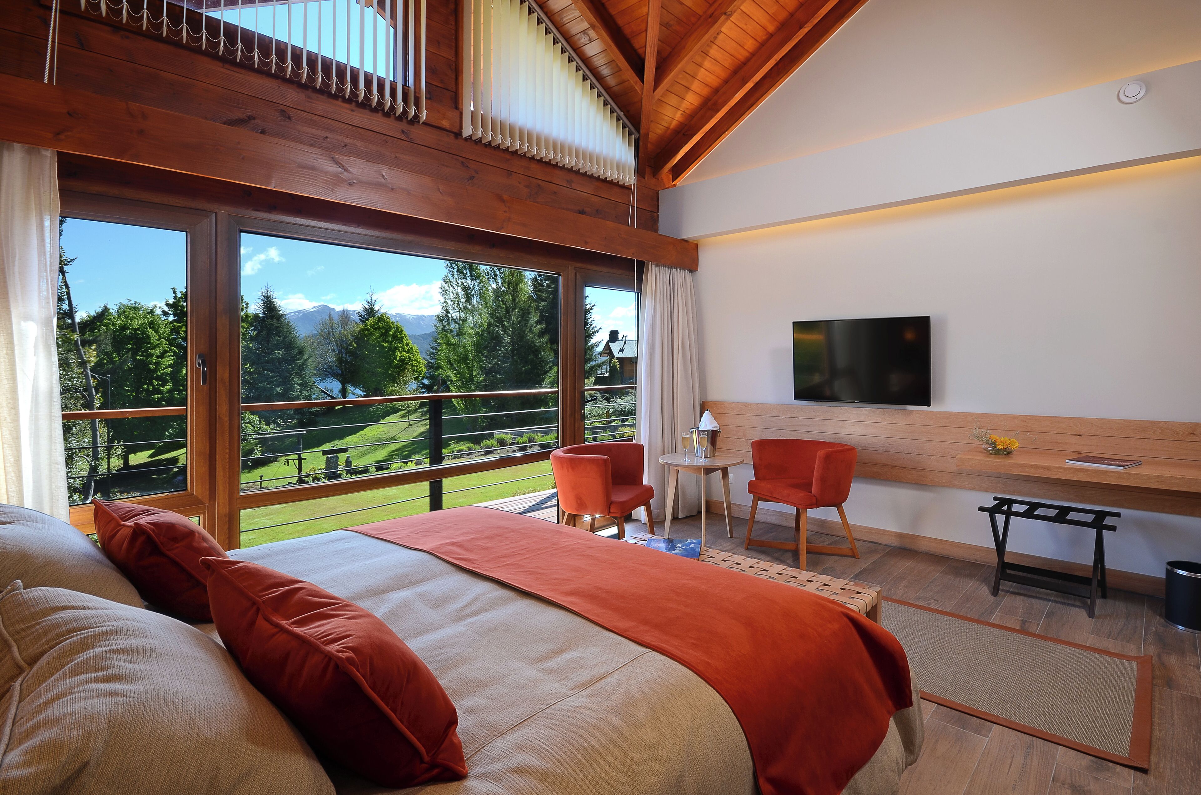 Un dormitorio con una cama grande, dos sillones, un televisor y vistas a un paisaje verde.