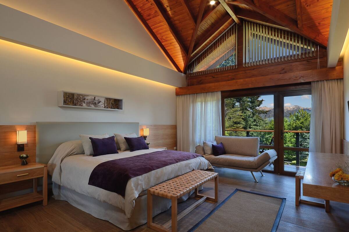 Une chambre à coucher comprenant un lit, des tables de chevet, un banc, un canapé et une vue sur l’extérieur.