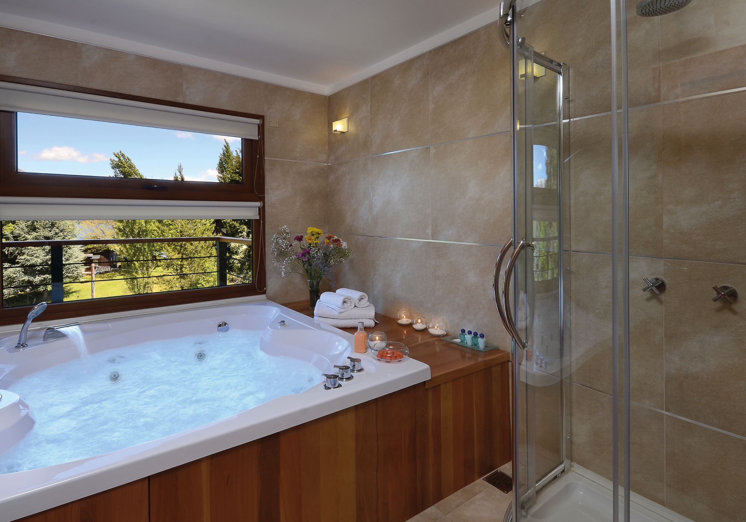 Un bagno con una vasca da bagno ampia, un box doccia in vetro e una finestra vista alberi.