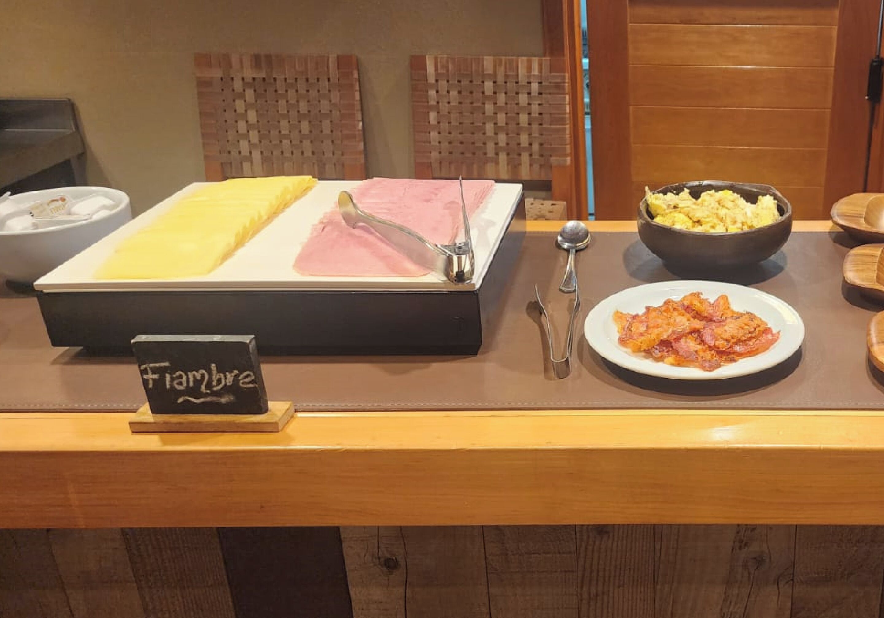 Un bufé de desayuno con un letrero que dice "Fiambre", que ofrece una variedad de platos, incluyendo huevos revueltos, jamón y un plato de pasta.