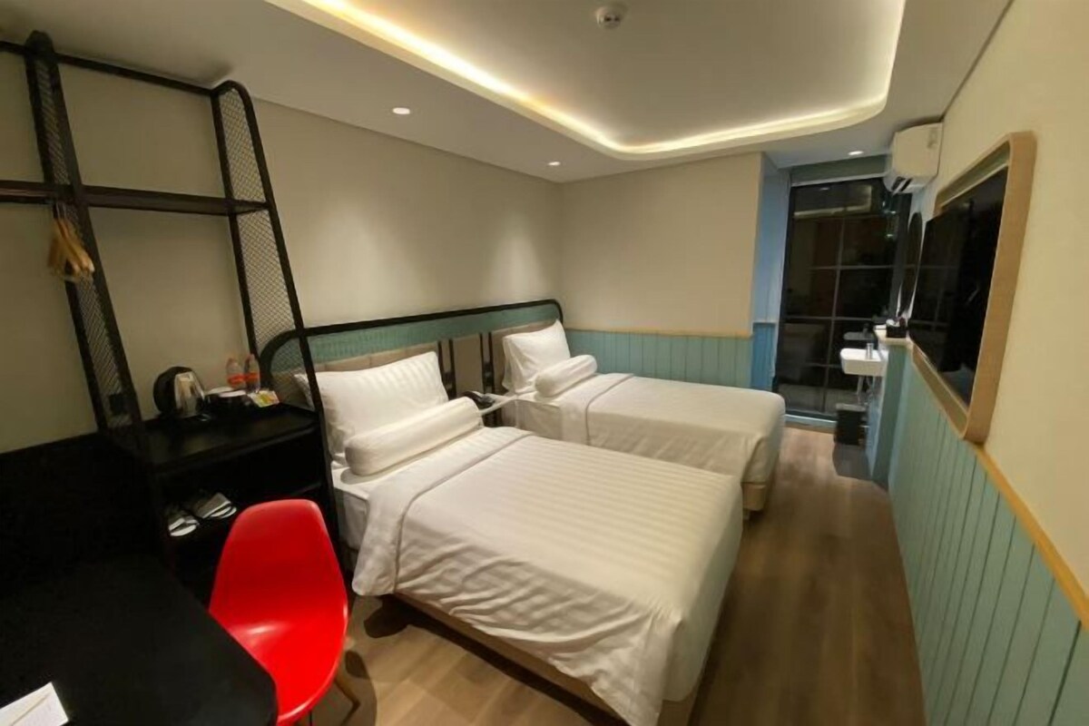 A hotel room with two beds, a desk, a red chair, and a mirror.