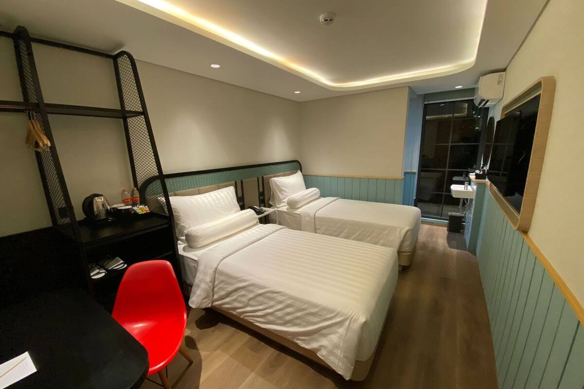 A hotel room with two beds, a desk, a red chair, and a mirror.