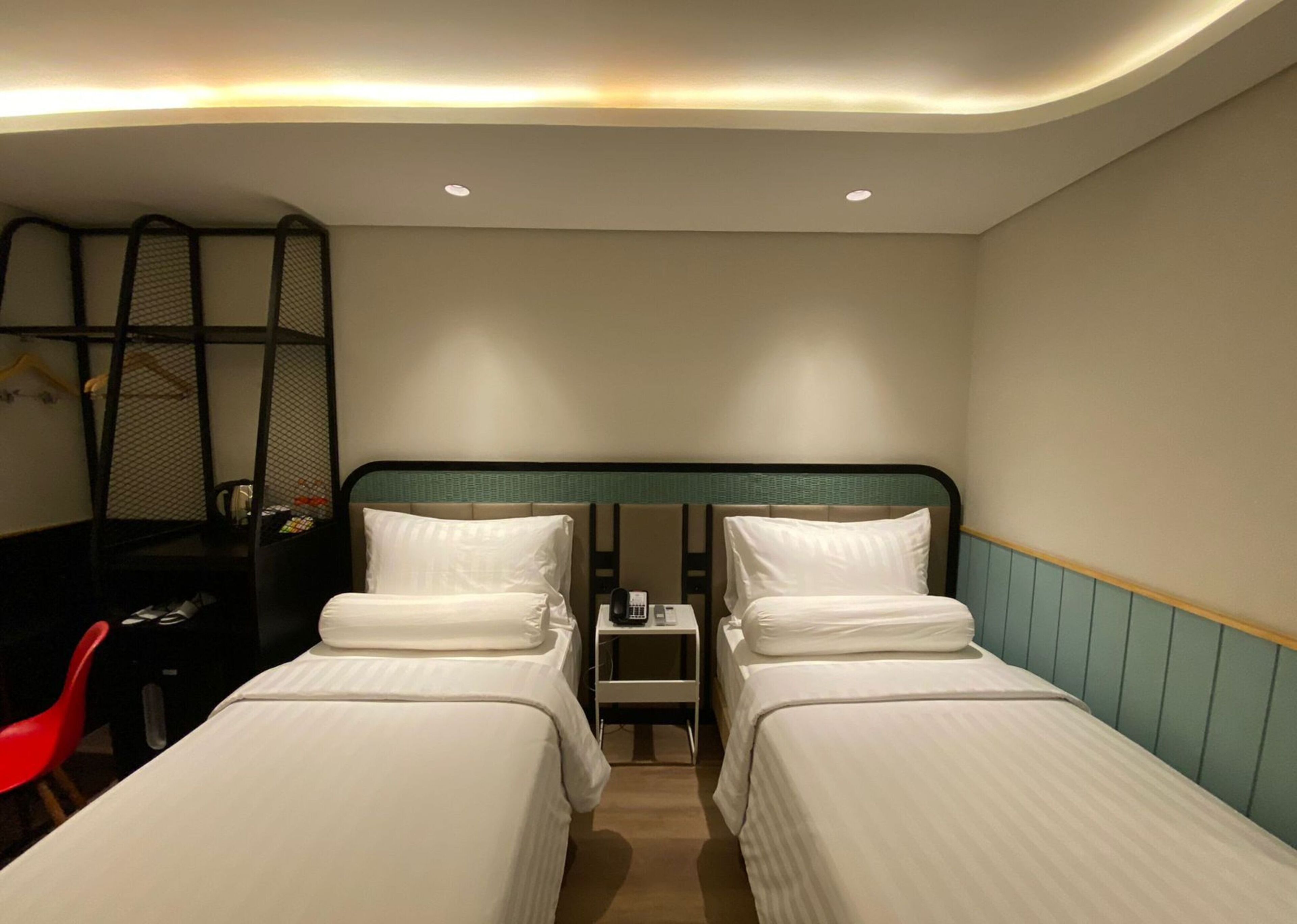 A hotel room with two single beds, a desk with a chair, a small table with a phone, and a red chair.