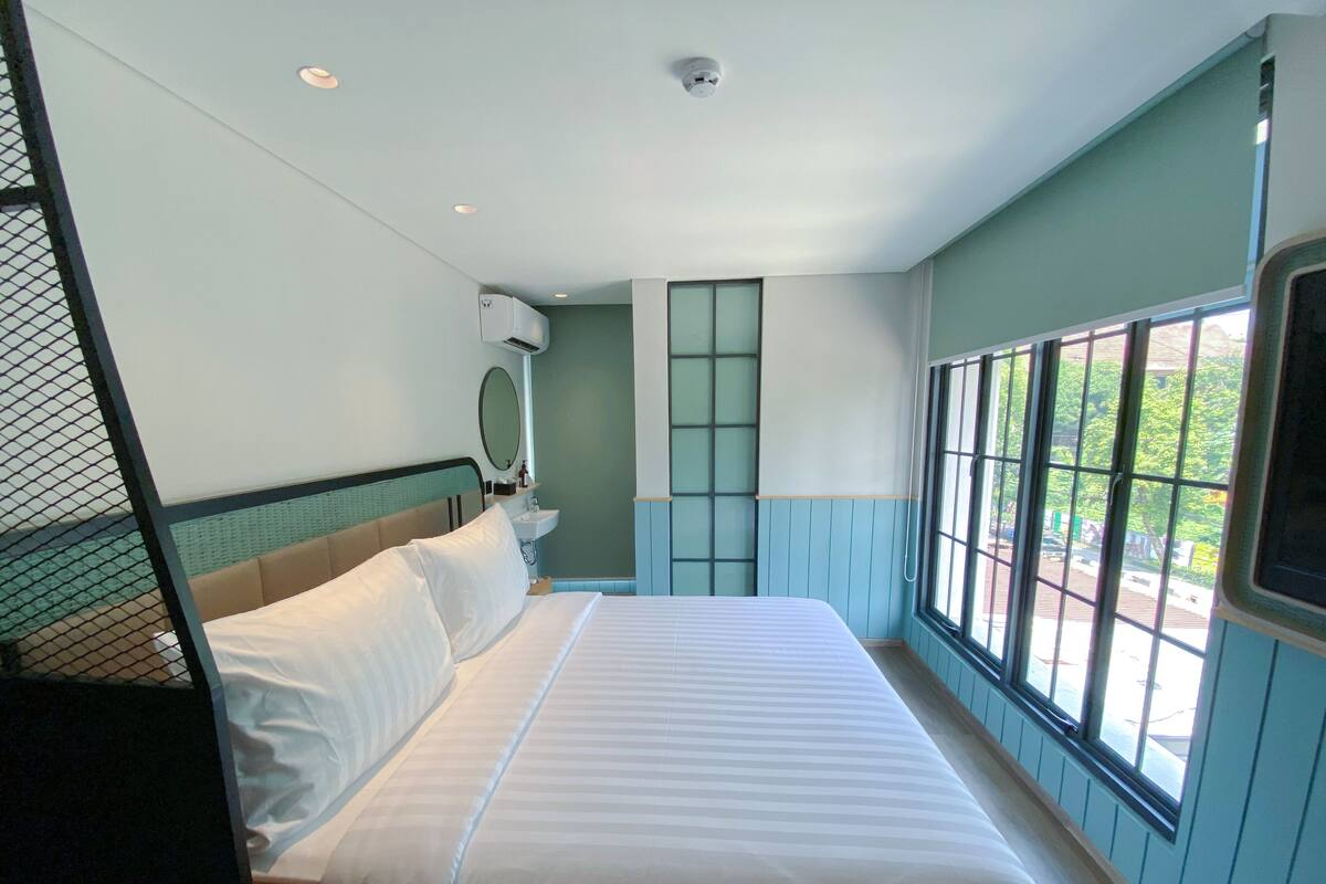 A hotel room with a bed, a window, and a wall-mounted air conditioner.