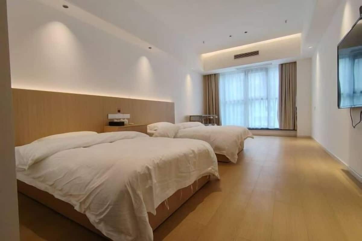 A hotel room with two beds, a flat-screen TV, and a large window with curtains.