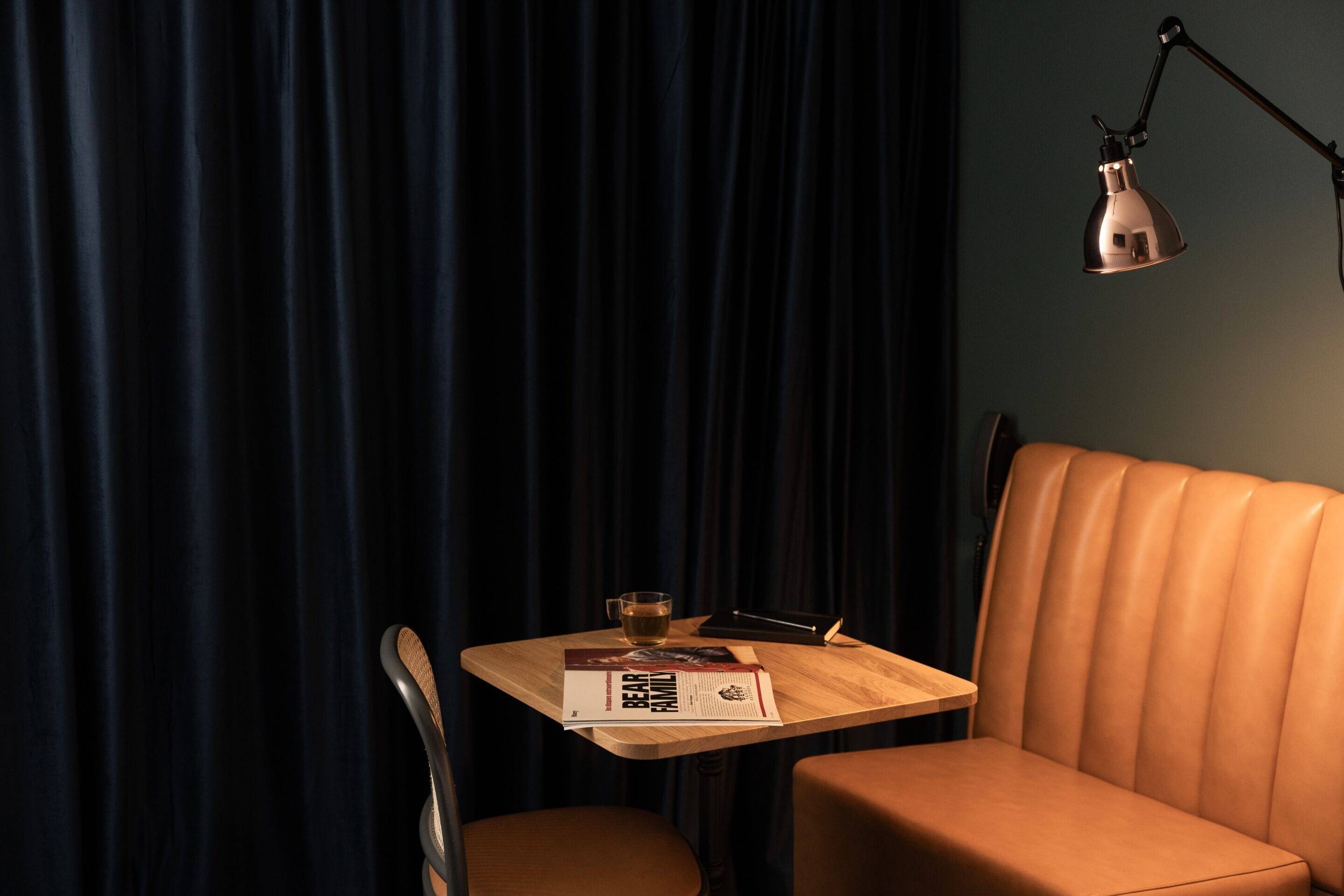 A small table with a book, a glass of water, and a cup, set against a dark curtain backdrop.