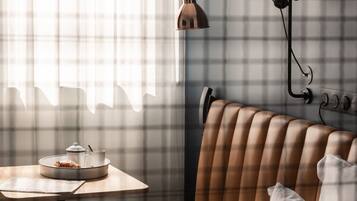 Una habitación acogedora con una pared a cuadros, un banco de cuero marrón, una mesa con lámpara y una ventana con cortinas traslúcidas.
