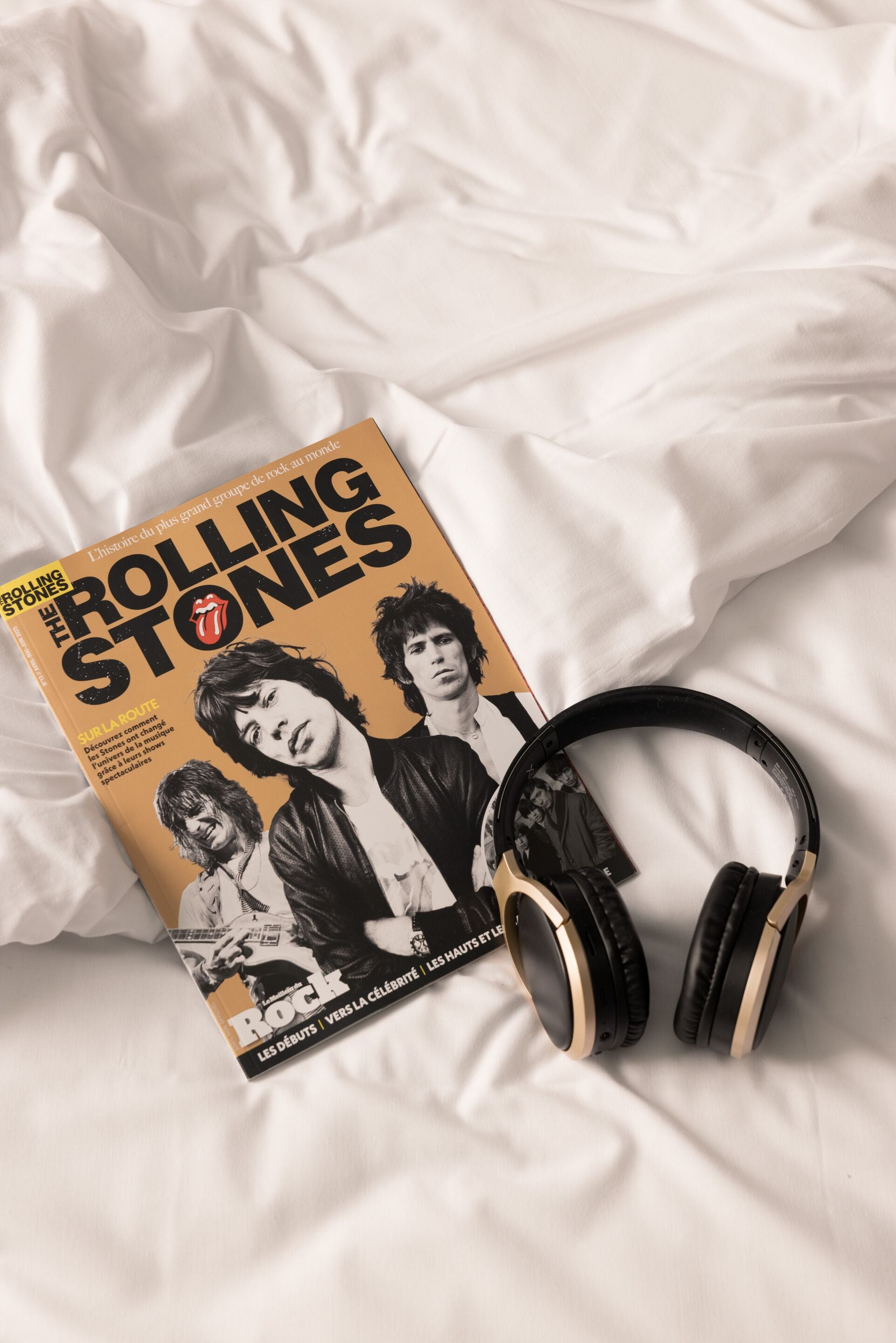 Una revista con el título 'Rolling Stones' y un par de auriculares sobre una superficie de tela blanca.