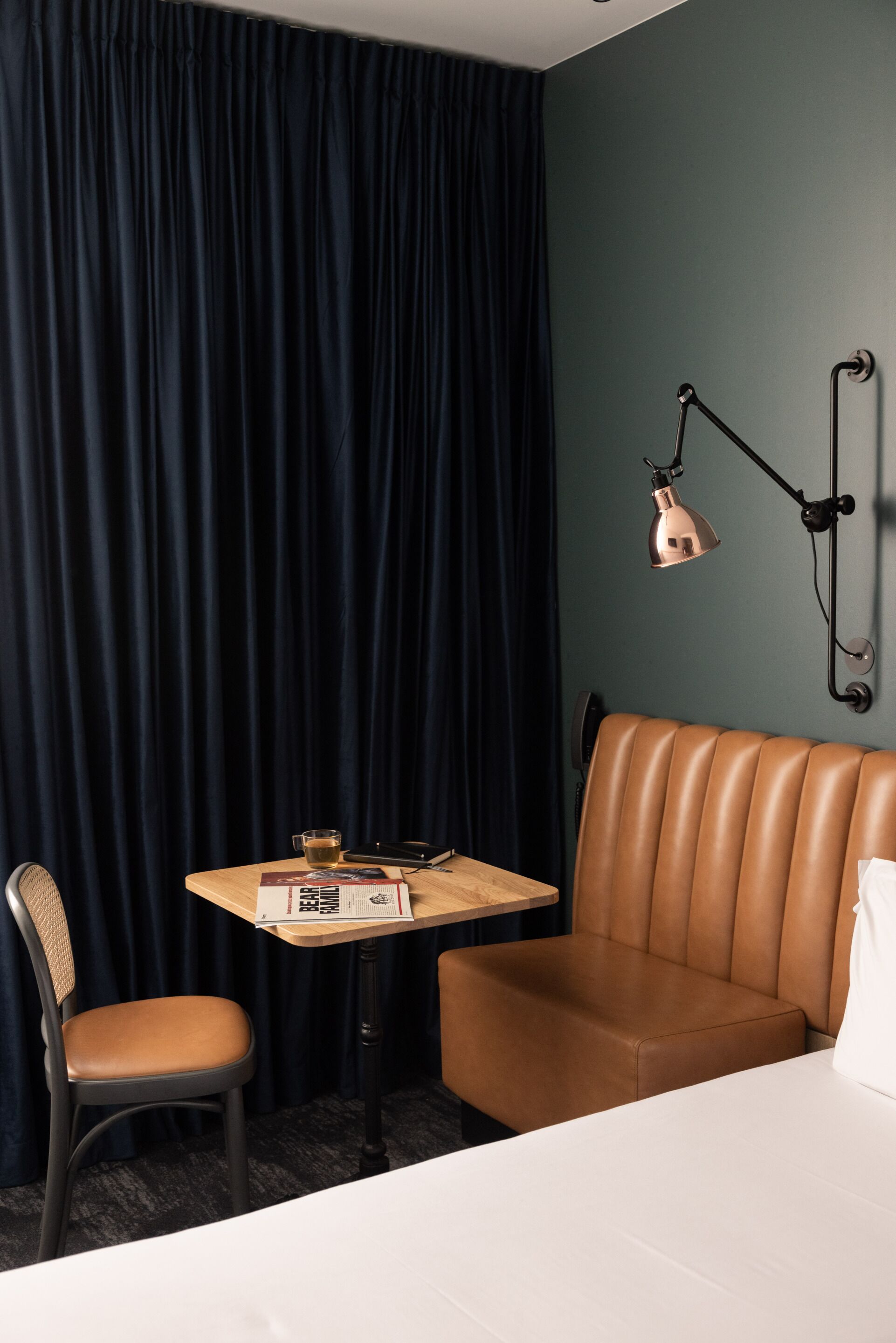 Une chambre d’hôtel avec un canapé en cuir marron, une table en bois sur laquelle se trouve un verre, une chaise et une lampe.