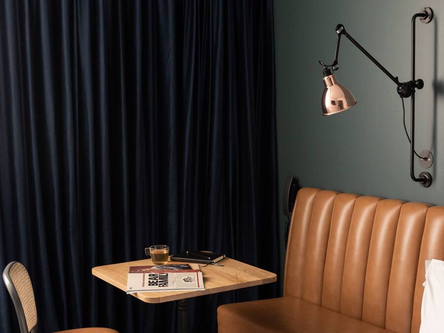 Une chambre d’hôtel avec un canapé en cuir marron, une table en bois sur laquelle se trouve un verre, une chaise et une lampe.