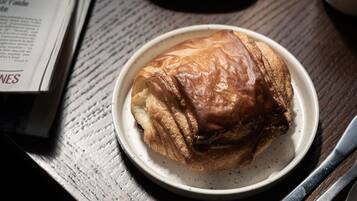 Ein Holztisch mit einem Croissant, einem Teller mit einem Ei, einer Marmeladenglas und einer Zeitung.
