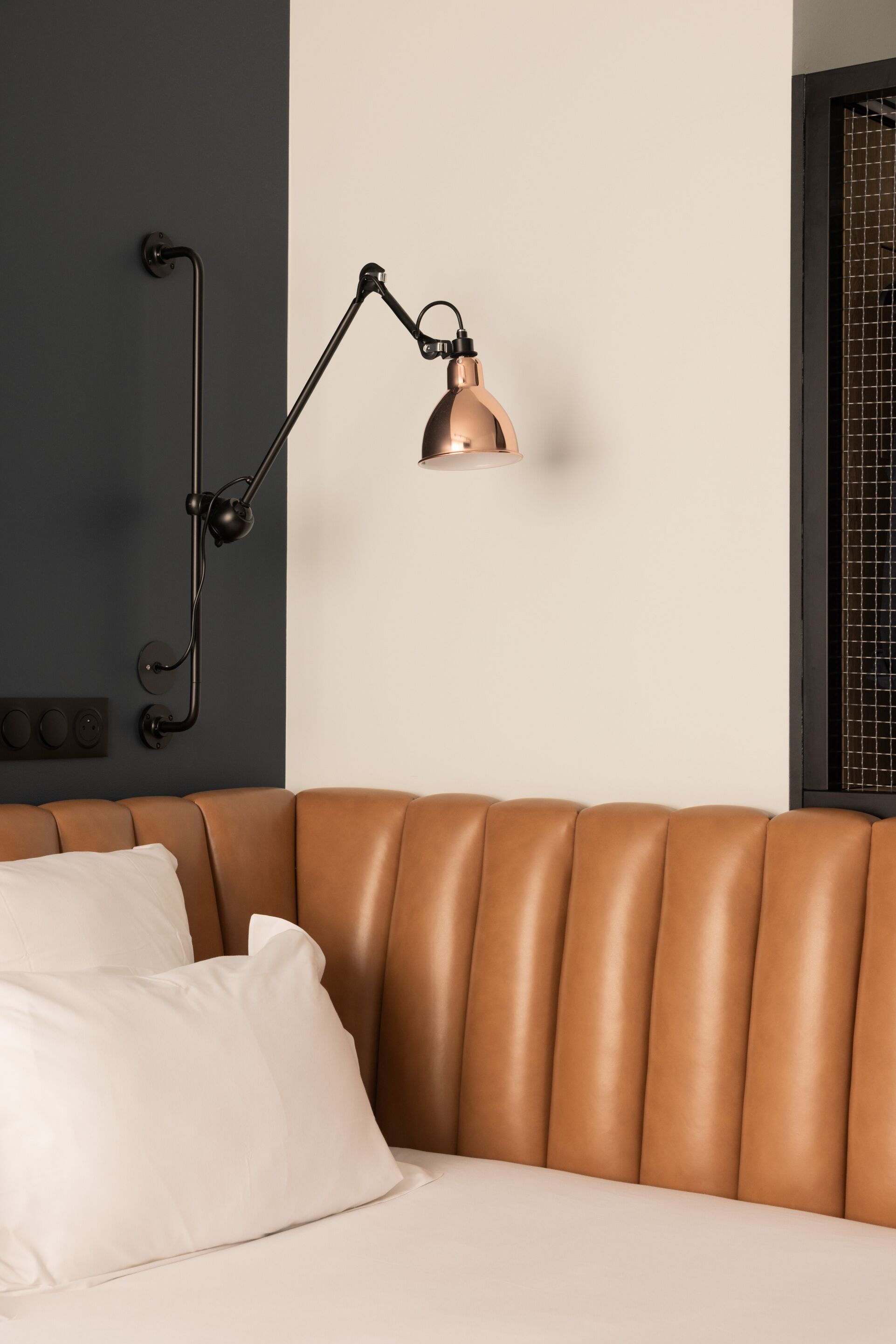 Ein modernes Schlafzimmer mit einem Leder-Kopfstueck, einer Wandlampe und einem weißen Kissen.