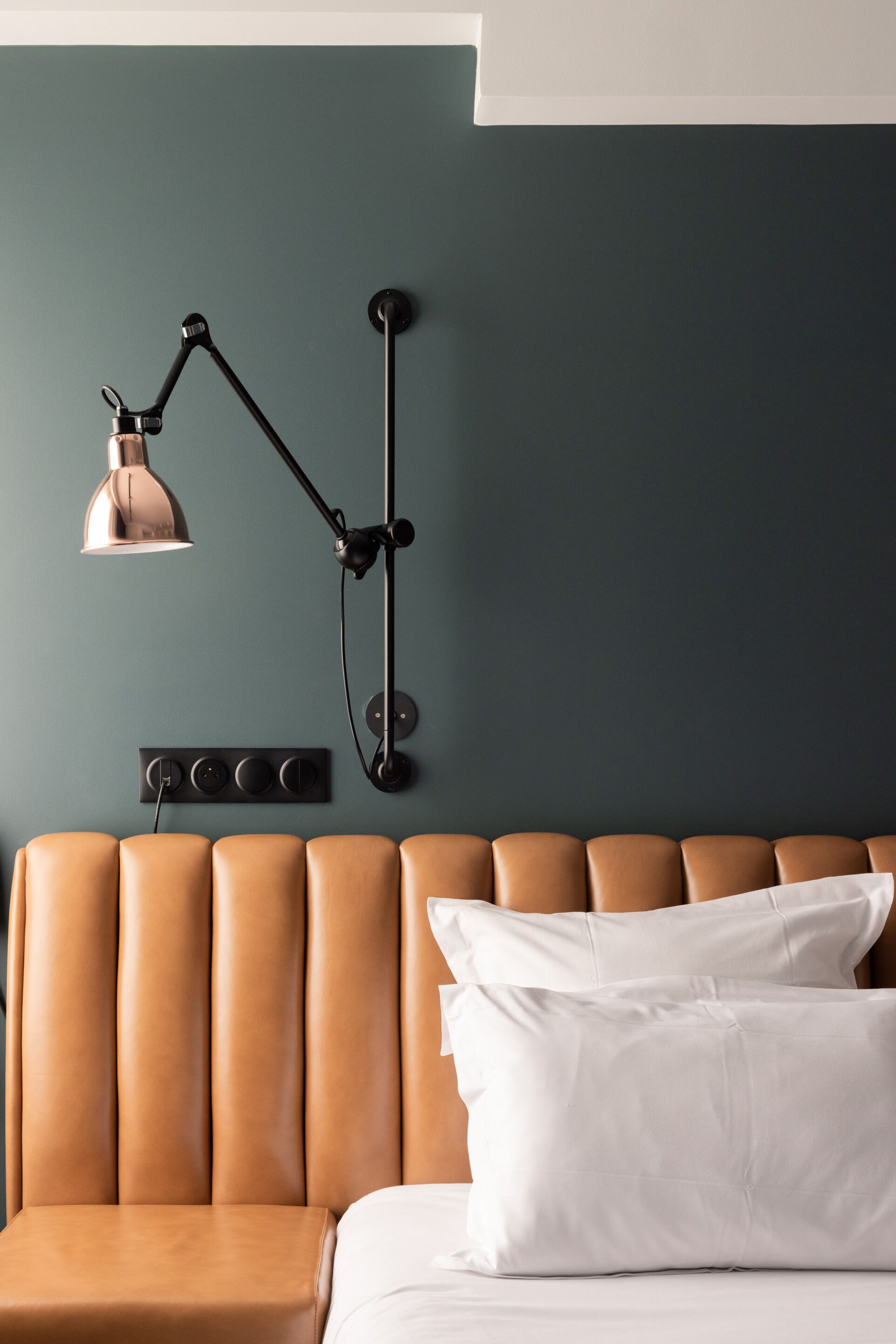 Una habitación con cabecera de cuero marrón, almohada blanca y lámpara de escritorio negra.