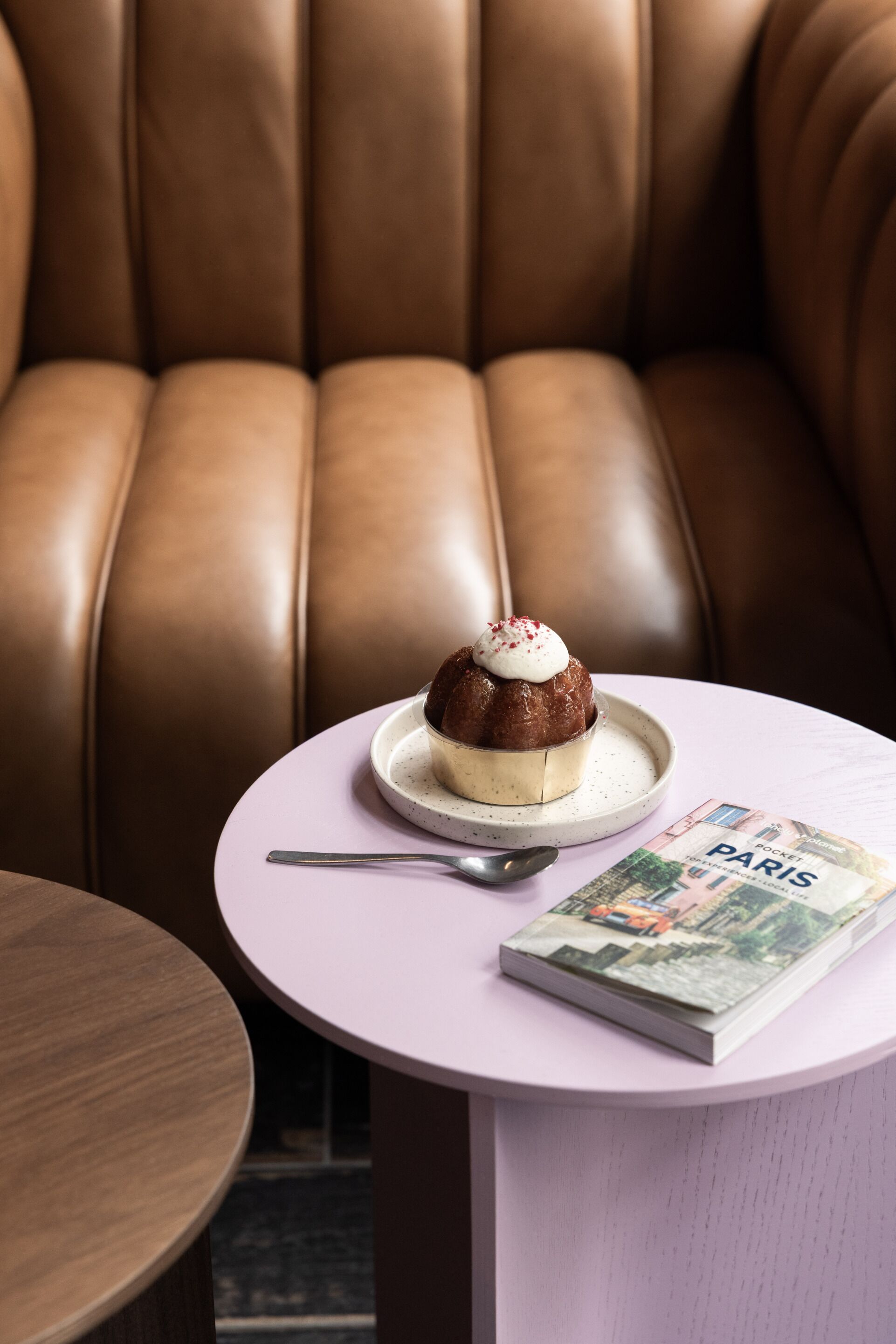 A round table with a dessert on a plate, a spoon, and a magazine titled "PARIS".