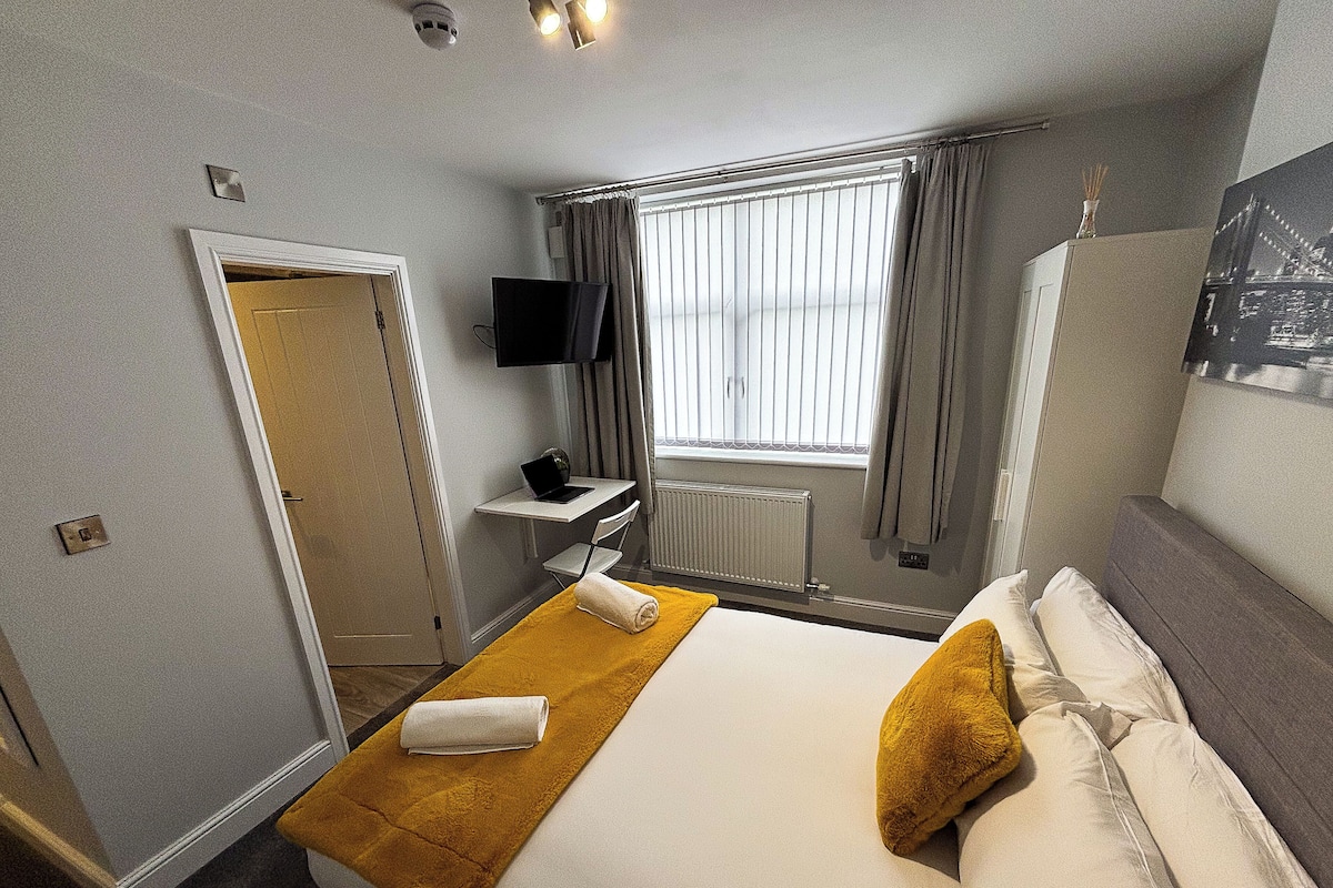 Ein Hotelzimmer mit Bett, Schreibtisch, Laptop, Fernseher und einem Fenster mit Vorhängen.