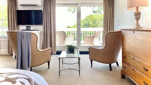 A hotel room with a bed, two armchairs, a small table, a dresser, a TV, and a balcony with wicker furniture. - Old Village Inn - King Room (Ogunquit)