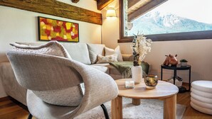 Una sala de estar acogedora con un sofá, una mesita redonda con velas, un jarrón con flores secas y vistas a la montaña a través de una ventana.