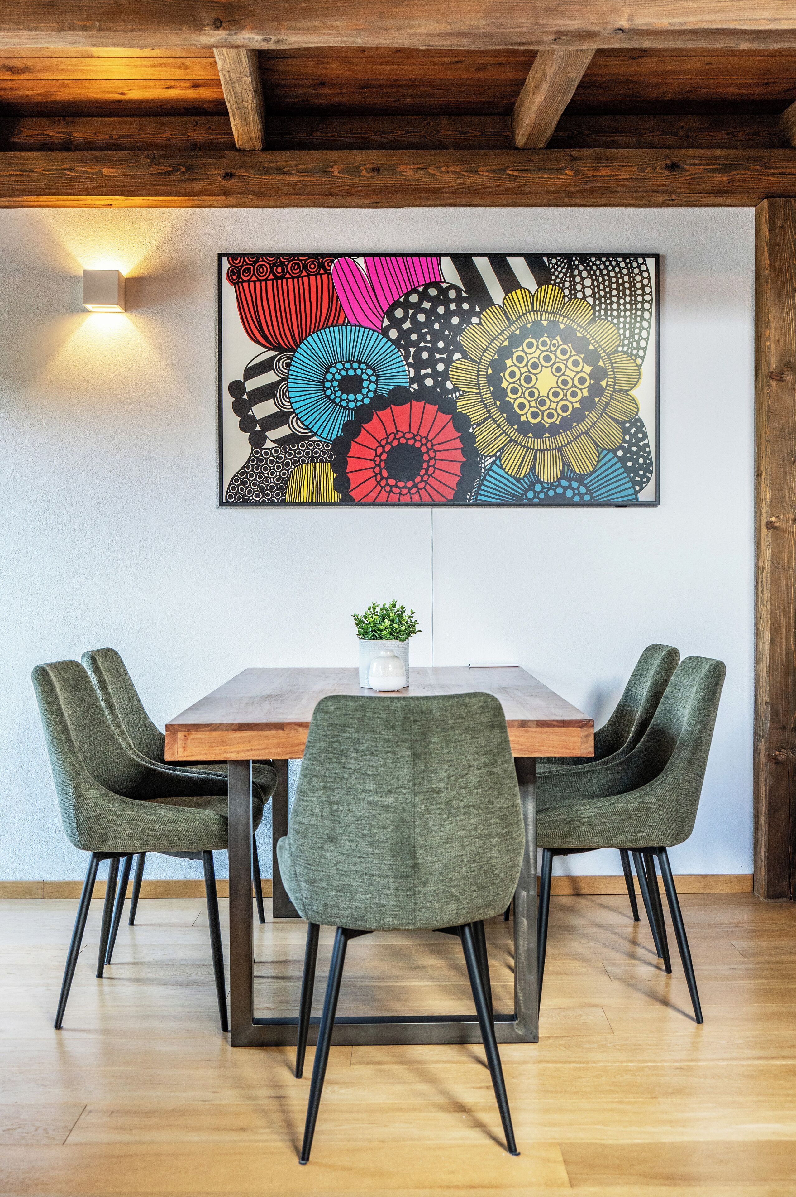 A dining area with a wooden table, four upholstered chairs, and a colorful abstract painting on the wall.