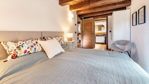 Un dormitorio con una cama grande, vigas de madera en el techo, una mesita de noche con lámpara y una silla.