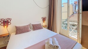 A hotel room with a bed, two wall-mounted lamps, a window with curtains, and a view of the outside balcony. - N&J - CITY TRIP - Central - Balcony (Niza)