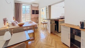 A modern kitchen with a wooden countertop and a coffee machine, a dining area with a table and chairs, and a large window with curtains. - N&J - CITY TRIP - Central - Balcony (Niza)