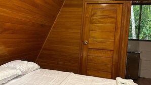 Un dormitorio con techo inclinado de madera, cama con ropa de cama blanca y una puerta de madera.