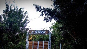 Un letrero que indica 'El Trápiche', con un número de contacto y una puerta de madera.