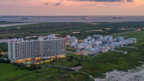Ein großes Hotel mit mehreren Gebäuden, ein Strand im Vordergrund und Schiffe in der Ferne.