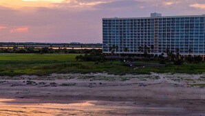 Ein Hotel im modernen Stil, gelegen in Strandnähe mit Blick auf das Meer und einem Sonnenuntergang im Hintergrund.