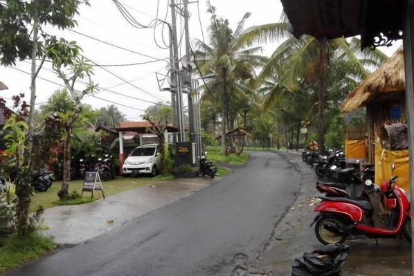 A street with parked motorcycles and a red scooter, a white car, and a building with a signboard. - Duana Sari by Mahaputra (Bali)
