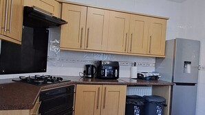 A kitchen with wooden cabinets, a gas stove, a coffee maker, a refrigerator, and a trash bin. - MC Suites (Newcastle-upon-Tyne)