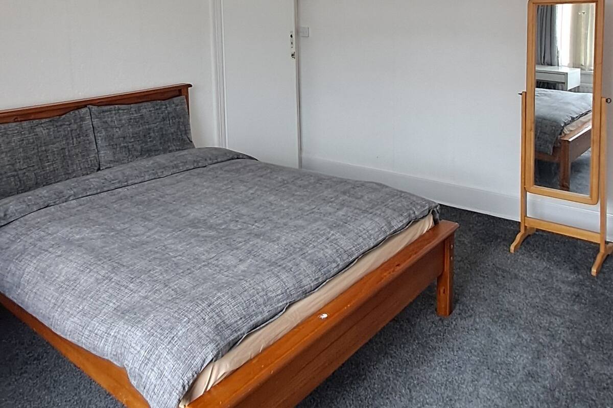 Une chambre à coucher avec un lit en bois, une moquette grise, une porte blanche et un miroir avec un cadre en bois.