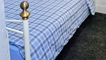 A bed with a white metal frame, blue and white checkered bedding, and a blue pillow.