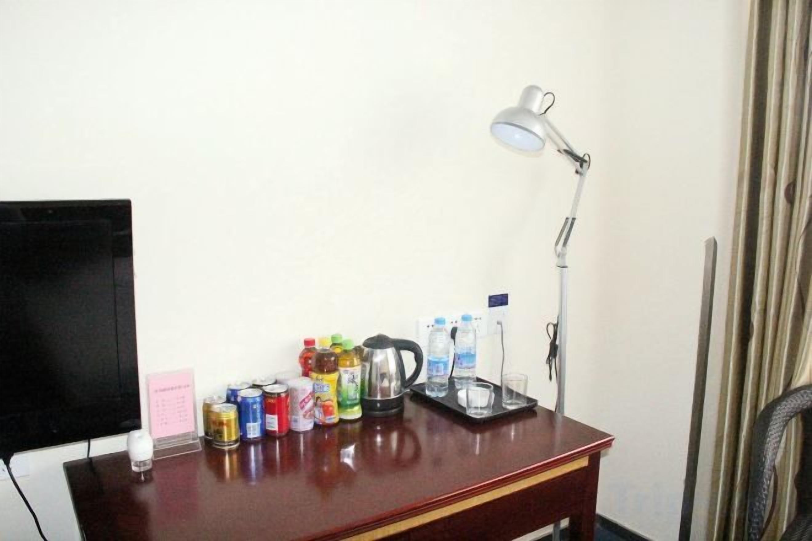 A desk with a lamp, a television, and various beverages.
