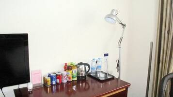 A desk with a lamp, a television, and various beverages.