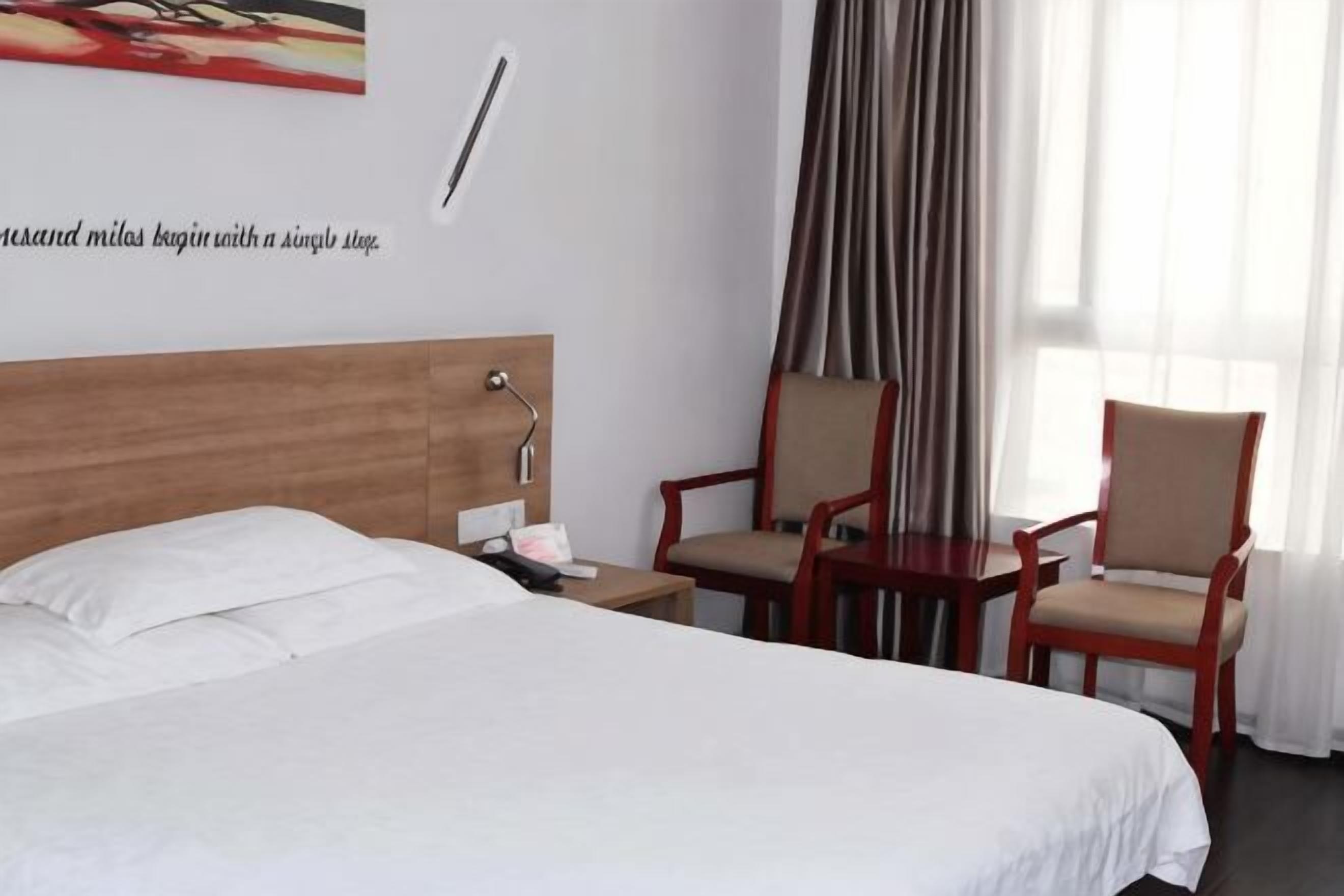A hotel room with a bed, two chairs, a nightstand, a wall clock, and a window with curtains.