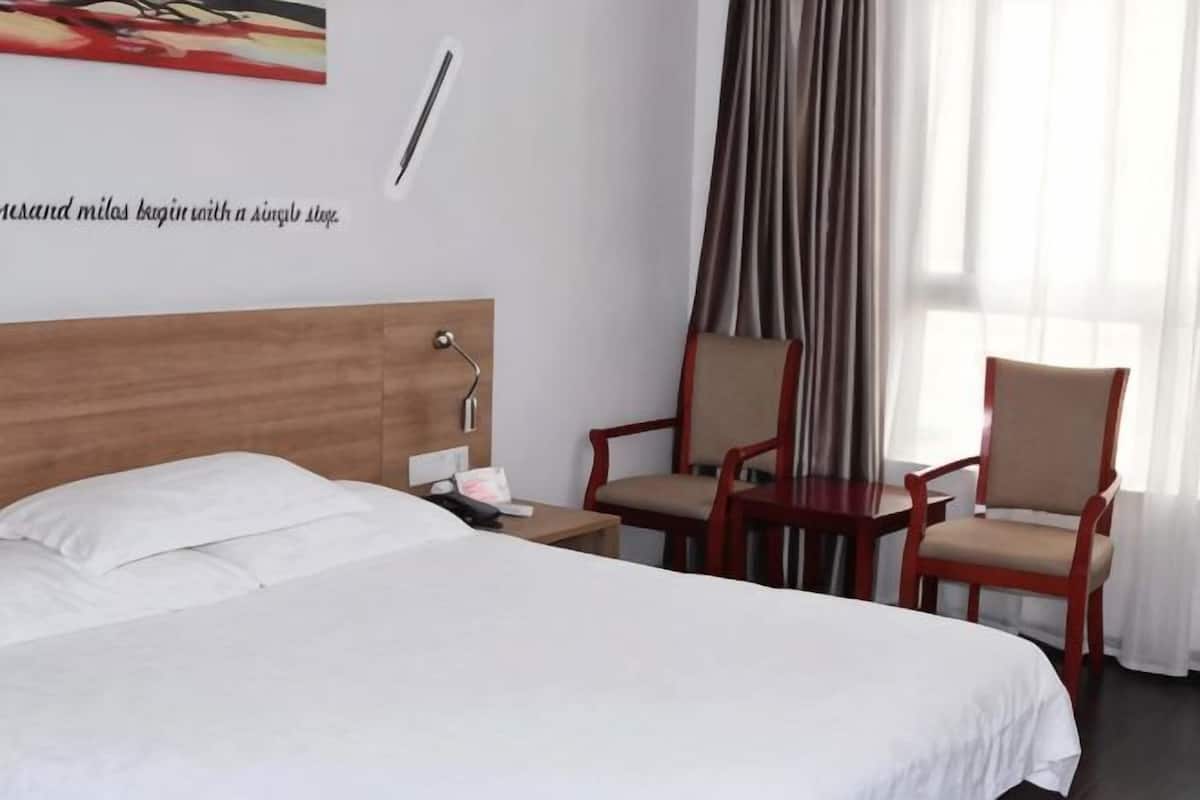 A hotel room with a bed, two chairs, a nightstand, a wall clock, and a window with curtains.