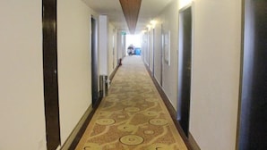 Corredor de hotel com carpete estampado, portas em ambos os lados e teto com design texturizado.