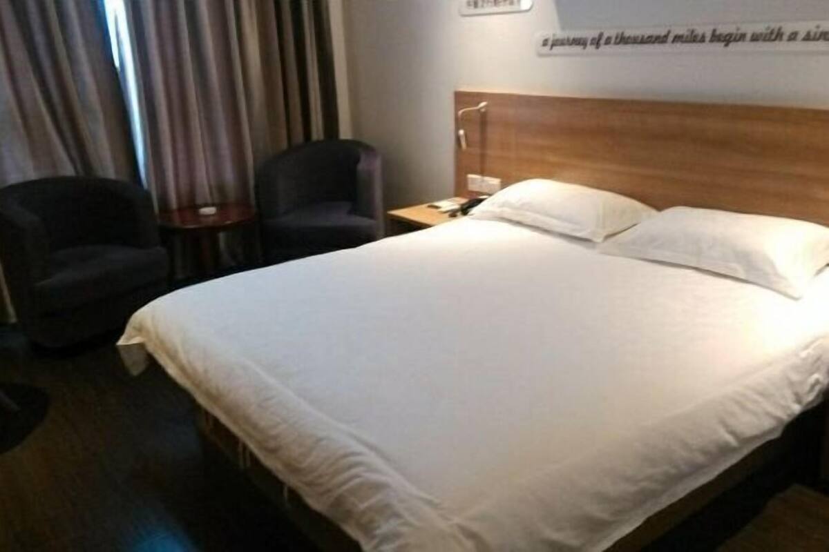 A hotel room with a bed, two chairs, a nightstand, and a wall with a motivational quote.
