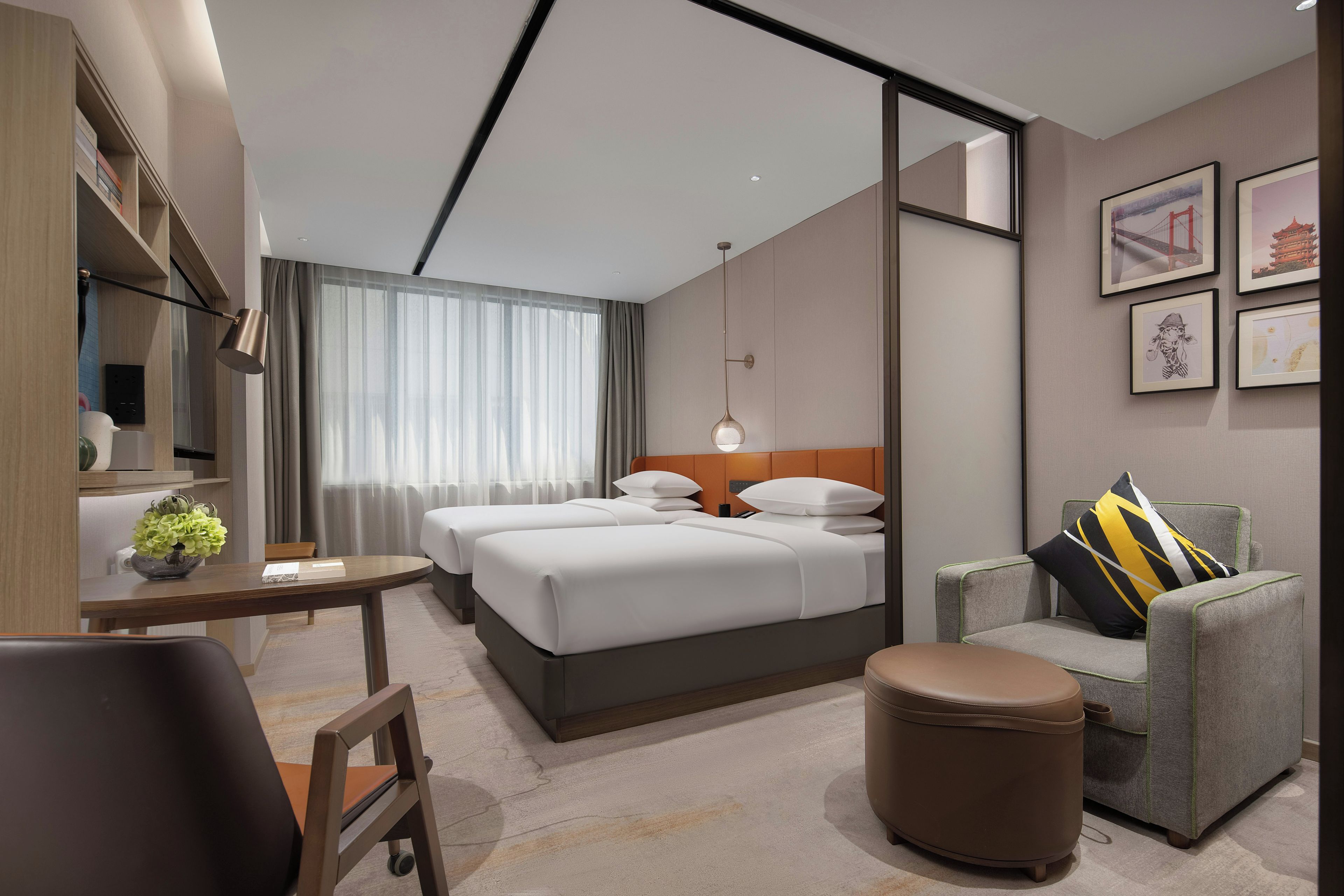 Una habitación de hotel moderna con una cama grande, un escritorio, una silla, una mesita con una planta, un sofá con cojines decorativos y un televisor de pared.
