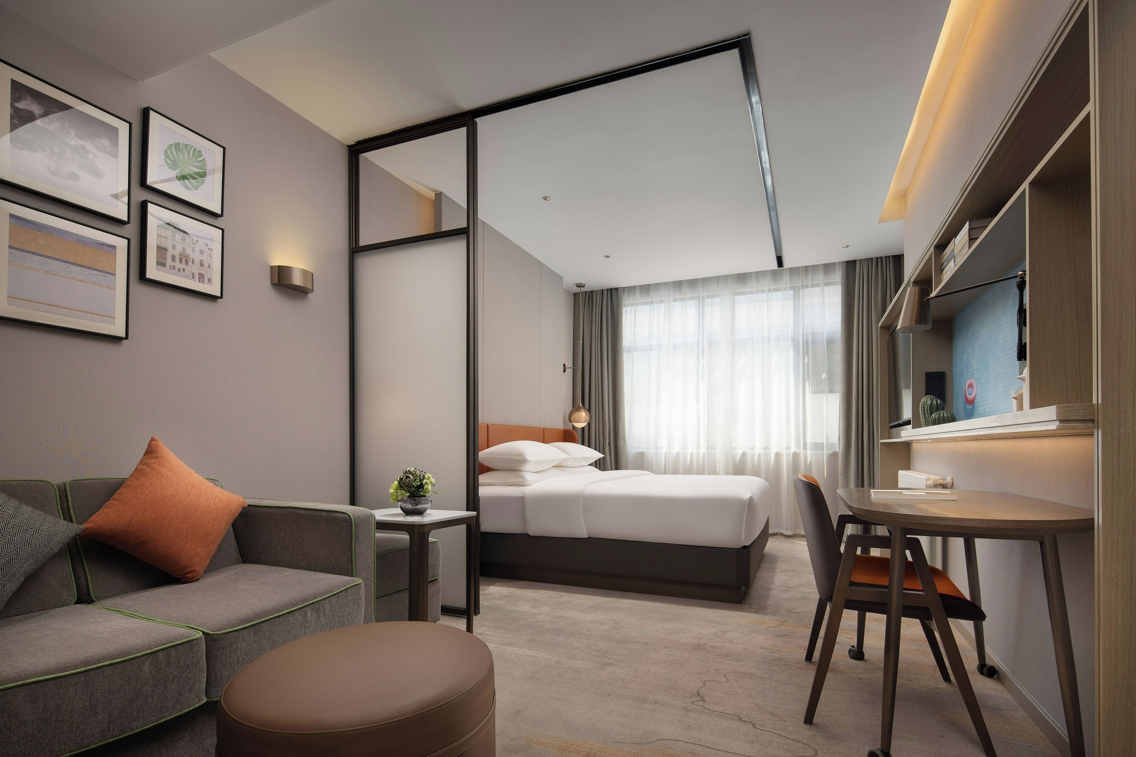 A modern hotel room with a bed, a desk, a sofa, and a mirror.