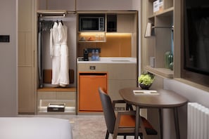 Habitación de hotel compacta con kitchenette, un pequeño comedor, baño y armario con batas.