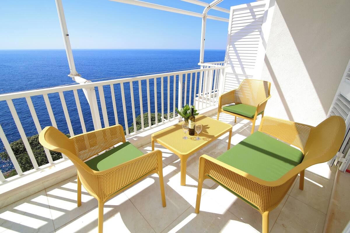 A balcony with a view of the ocean, featuring wicker furniture and a small table with a bottle and glasses.