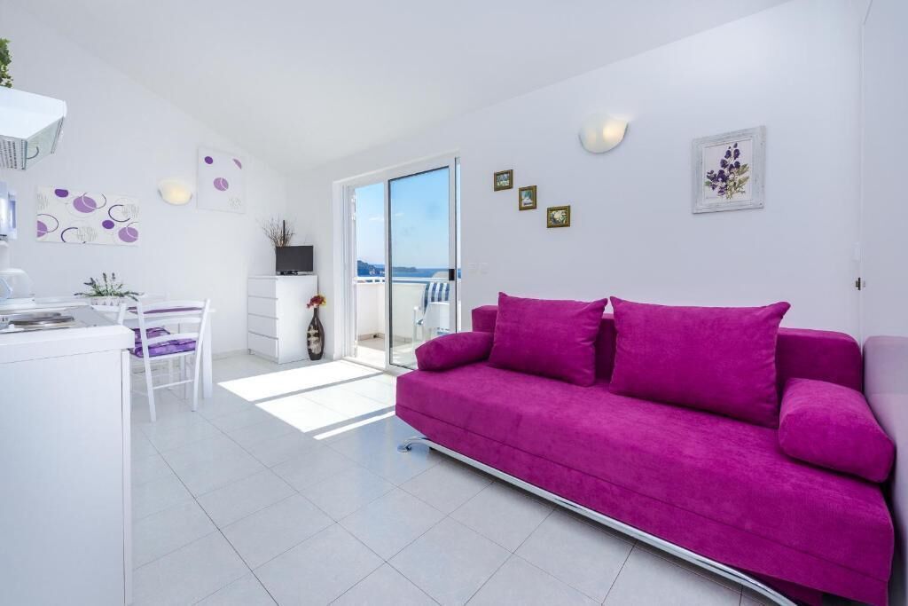 A modern living room with a bright white color scheme, a purple sofa, and a glass door leading to a balcony.