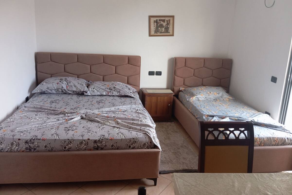 A bedroom with two beds, a nightstand, a small table, and a wall-mounted air conditioner.
