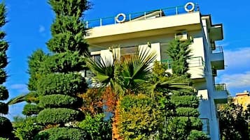 A modern building with balconies, surrounded by well-maintained greenery and a clear blue sky.