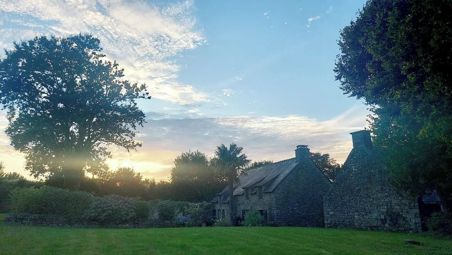A stone building with a thatched roof, surrounded by lush greenery and trees.